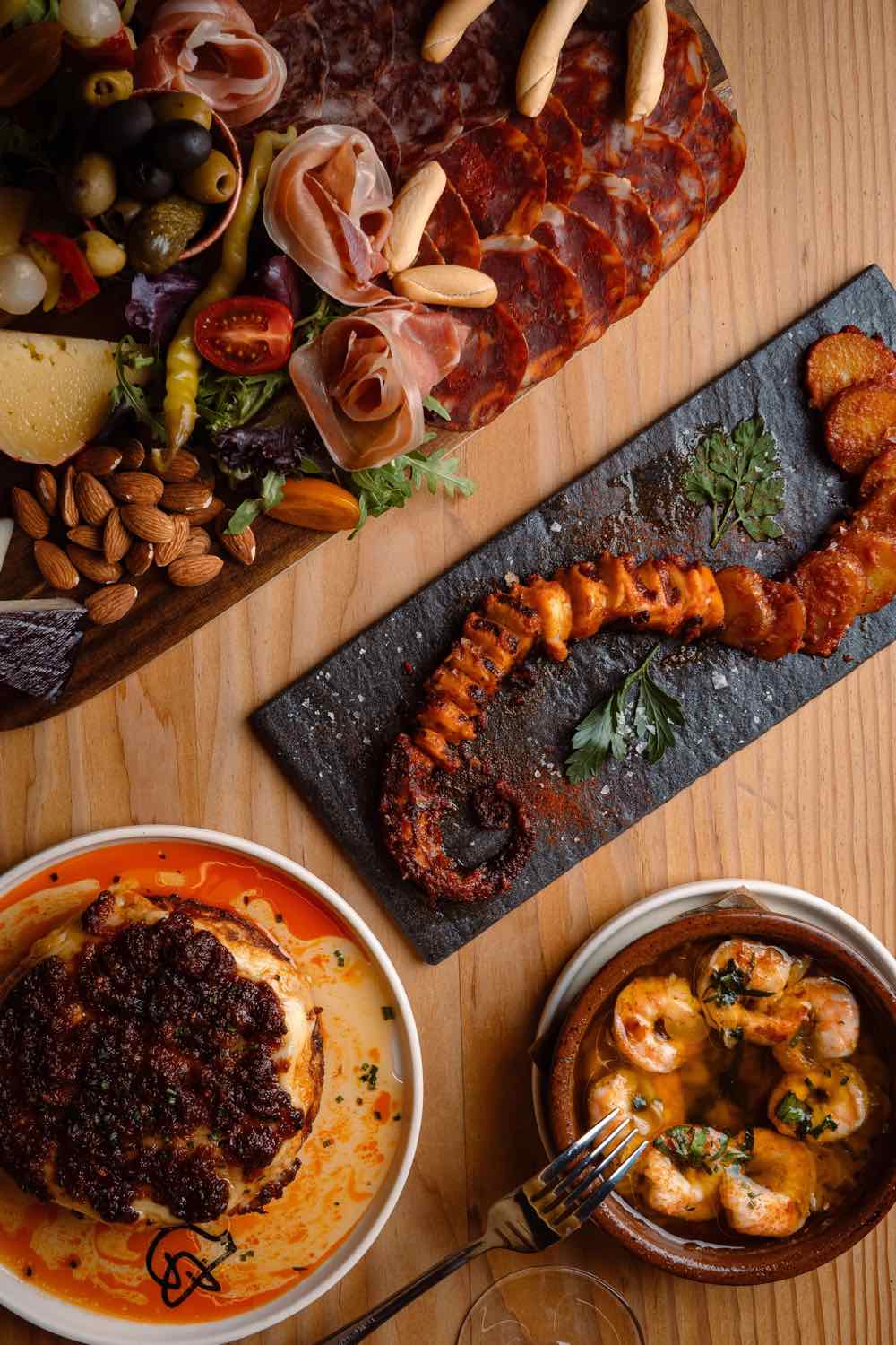 A long slate board of Spanish charcuterie, olives and warm tapas at Piggs