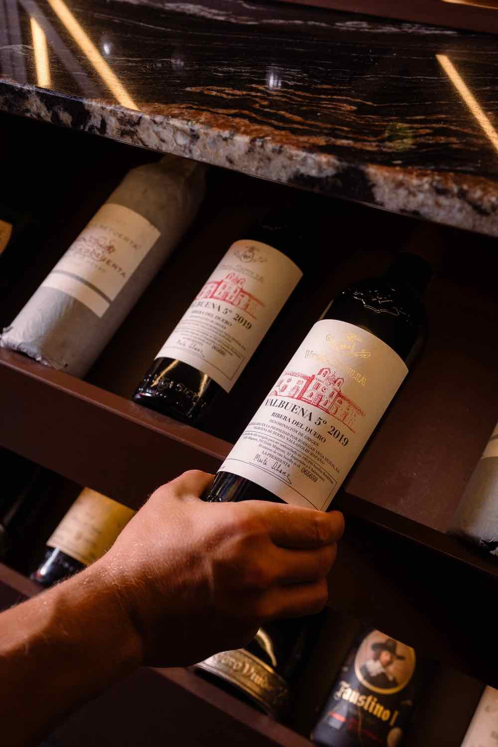 A hand choosing a bottle from the Piggs wine rack