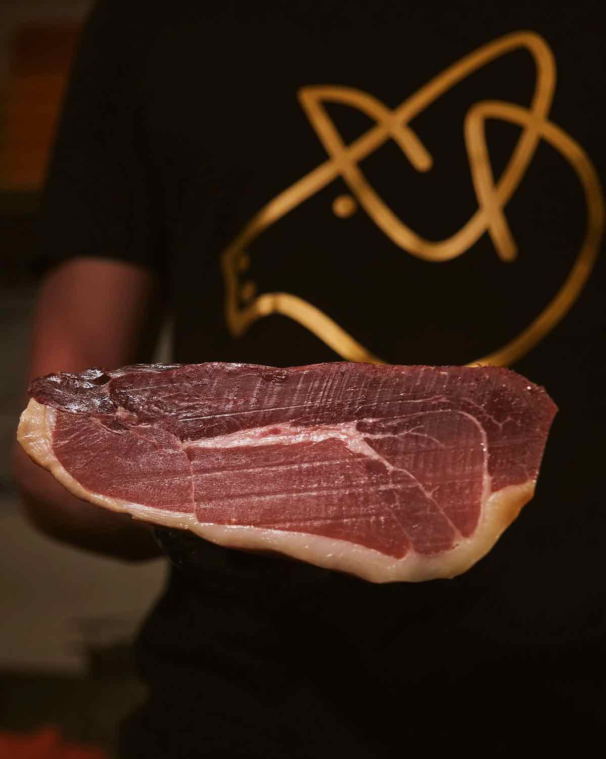 A hand holding a slice of Spanish jamón at Piggs