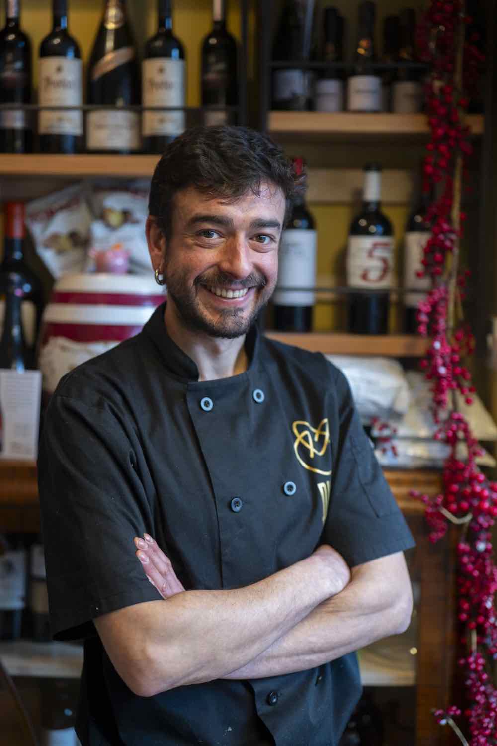 Head chef Chevi in chef whites in front of the wine bottles at Piggs